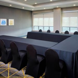 Hotel meeting room with three tables arranged in a U-shape and seating for over a dozen attendees.