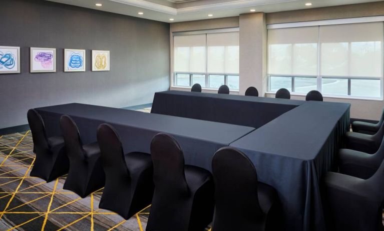 Hotel meeting room with three tables arranged in a U-shape and seating for over a dozen attendees.