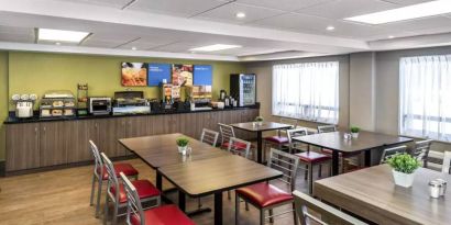 The hotel breakfast area has a hard floor, large windows, and tables for four to six diners.