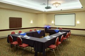 Meeting room with numerous tables, projector screen, and seating for around a dozen.