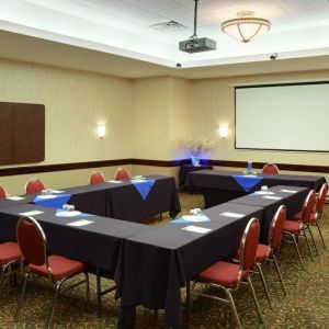 Meeting room with numerous tables, projector screen, and seating for around a dozen.