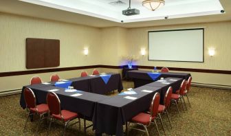 Meeting room with numerous tables, projector screen, and seating for around a dozen.