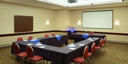 Meeting room with numerous tables, projector screen, and seating for around a dozen.