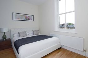 Hammersmith One’s bedroom, with double bed, bedside lamp, and nearby window.