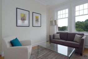 Living room with armchair, sofa, windows, and glass table.