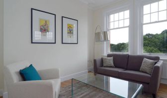 Living room with armchair, sofa, windows, and glass table.