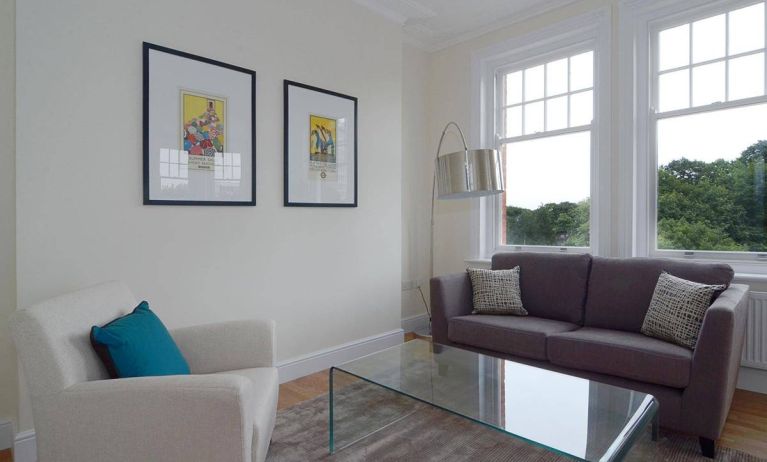 Living room with armchair, sofa, windows, and glass table.