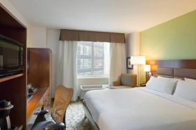 Hilton Garden Inn Midtown East guest room featuring large bed, big windows, and workspace chair and desk.