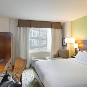 Hilton Garden Inn Midtown East guest room featuring large bed, big windows, and workspace chair and desk.