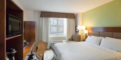 Hilton Garden Inn Midtown East guest room featuring large bed, big windows, and workspace chair and desk.