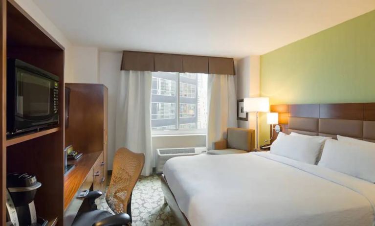 Hilton Garden Inn Midtown East guest room featuring large bed, big windows, and workspace chair and desk.