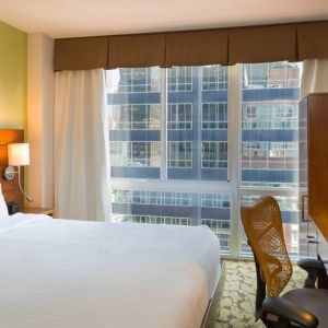 A Hilton Garden Inn Midtown East guest room with king-sized bed and floor-to-ceiling windows.