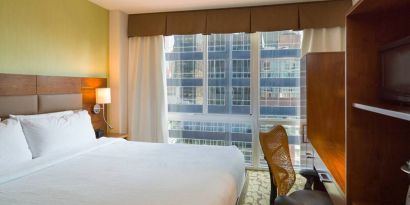 A Hilton Garden Inn Midtown East guest room with king-sized bed and floor-to-ceiling windows.