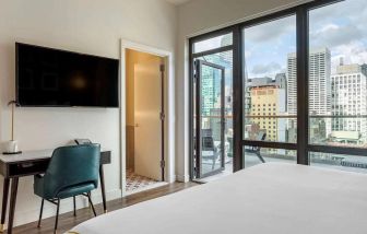 Guest room in The Draper, Ascend Hotel Collection, with TV and workspace desk and chair, plus city views.