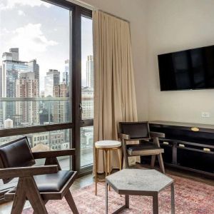 Guest room in The Draper, Ascend Hotel Collection, with two chairs, coffee table, large television, and urban vista through the window.