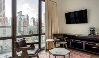 Guest room in The Draper, Ascend Hotel Collection, with two chairs, coffee table, large television, and urban vista through the window.