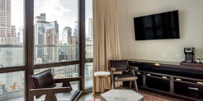 Guest room in The Draper, Ascend Hotel Collection, with two chairs, coffee table, large television, and urban vista through the window.