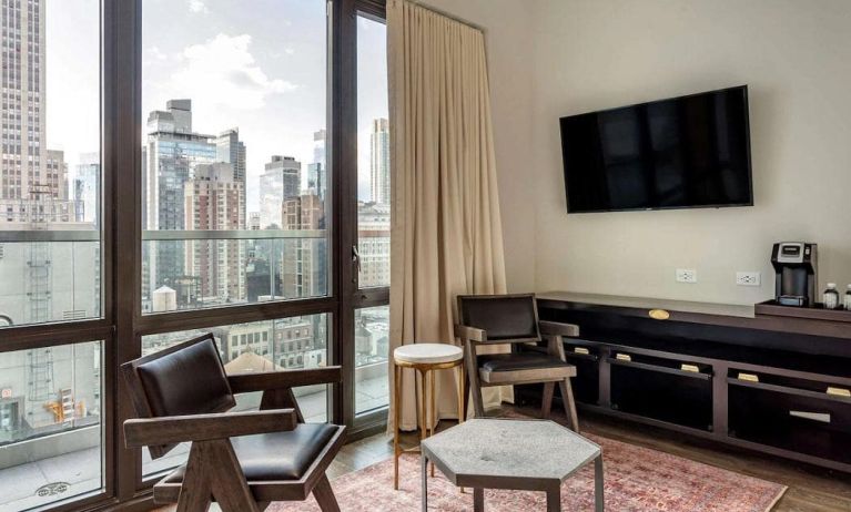 Guest room in The Draper, Ascend Hotel Collection, with two chairs, coffee table, large television, and urban vista through the window.