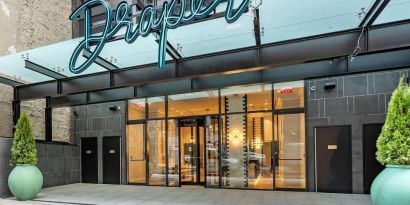 The hotel’s exterior, with The Draper, Ascend Hotel Collection’s name, awning, and large potted plants.