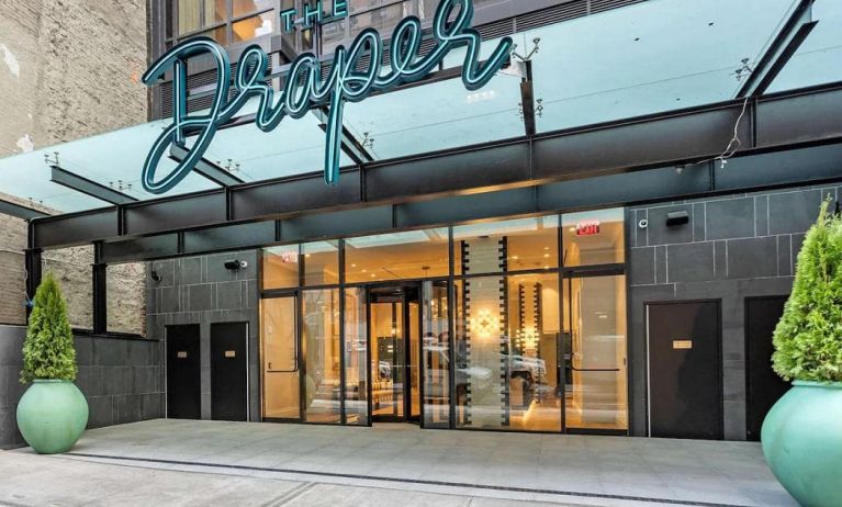 The hotel’s exterior, with The Draper, Ascend Hotel Collection’s name, awning, and large potted plants.