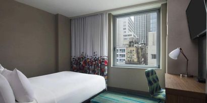 A single bed guest room in the Aloft Manhattan Downtown - Financial District, with TV and workspace desk and chair.