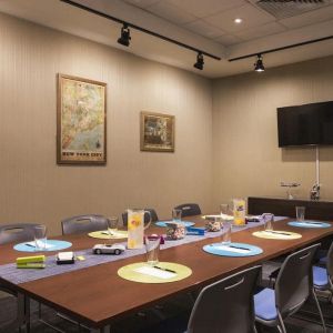 Meeting room with long wooden table, eight chairs, and nearby widescreen TV.