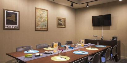 Meeting room with long wooden table, eight chairs, and nearby widescreen TV.