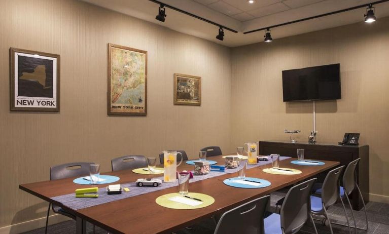 Meeting room with long wooden table, eight chairs, and nearby widescreen TV.