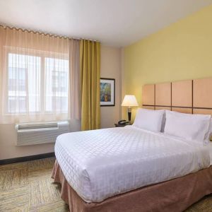 A guest room in the Candlewood Suites Times Square, with double bed, large TV, and window.