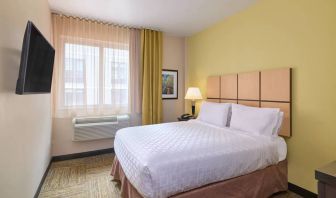 A guest room in the Candlewood Suites Times Square, with double bed, large TV, and window.