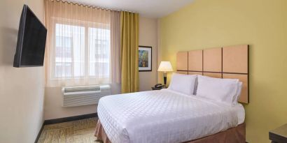 A guest room in the Candlewood Suites Times Square, with double bed, large TV, and window.