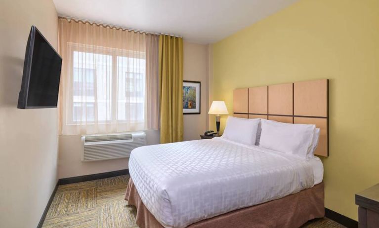 A guest room in the Candlewood Suites Times Square, with double bed, large TV, and window.