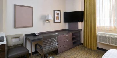 Workspace in a Candlewood Suites Times Square guest room, with desk, chair, TV, and window.