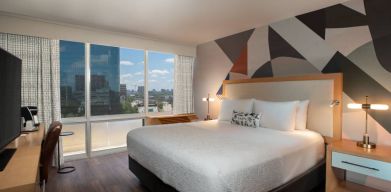 Double bed guest room in The Beeman Hotel, featuring large bed, and city view through the window.