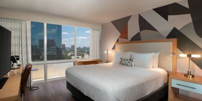 Double bed guest room in The Beeman Hotel, featuring large bed, and city view through the window.