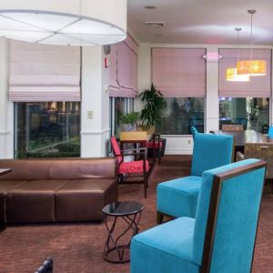 The lounge in the hotel lobby offers comfortable seating on chairs and sofas, with a large TV nearby.