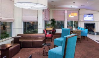 The lounge in the hotel lobby offers comfortable seating on chairs and sofas, with a large TV nearby.