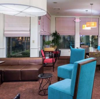 The lounge in the hotel lobby offers comfortable seating on chairs and sofas, with a large TV nearby.