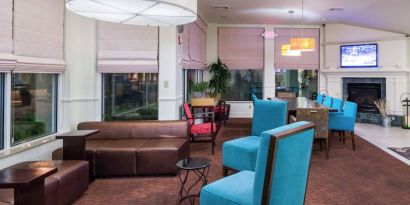 The lounge in the hotel lobby offers comfortable seating on chairs and sofas, with a large TV nearby.