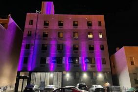 The hotel’s exterior is illuminated with purple lights and offers ample parking.