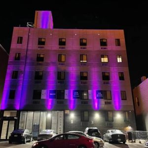 The hotel’s exterior is illuminated with purple lights and offers ample parking.