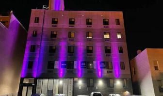 The hotel’s exterior is illuminated with purple lights and offers ample parking.