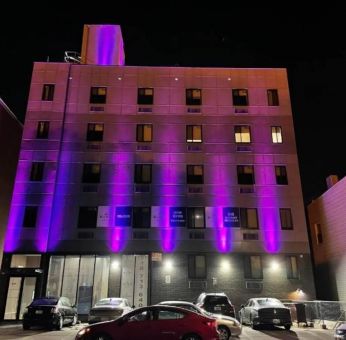 The hotel’s exterior is illuminated with purple lights and offers ample parking.