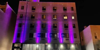 The hotel’s exterior is illuminated with purple lights and offers ample parking.