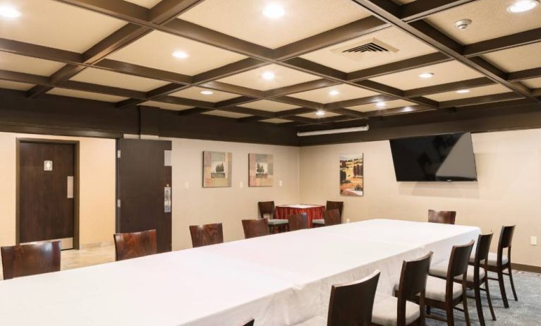 Hotel meeting room, featuring long table, surrounding chairs, and large TV.