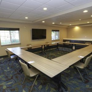 Hotel meeting room with four tables arranged in a square, and a large TV on the wall.