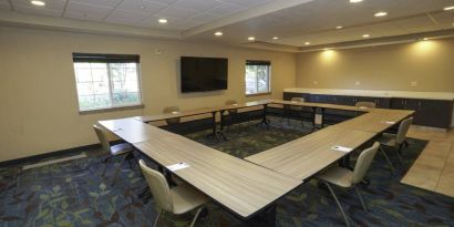 Hotel meeting room with four tables arranged in a square, and a large TV on the wall.