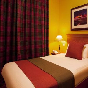 Single bed guest room in The Royal Highland Hotel, with bedside lamp and art on the wall.