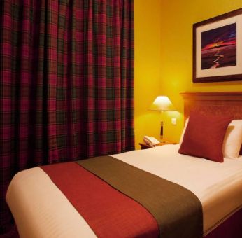 Single bed guest room in The Royal Highland Hotel, with bedside lamp and art on the wall.