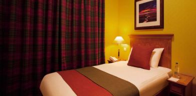 Single bed guest room in The Royal Highland Hotel, with bedside lamp and art on the wall.